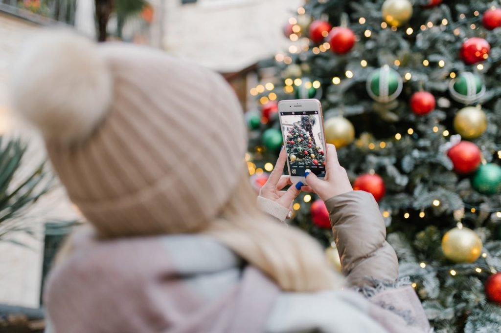A person taking a photo of a decorated Christmas tree with a smartphone outdoors.