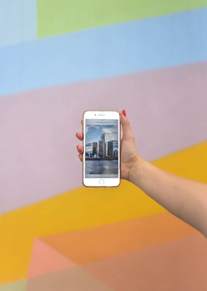 A hand holds a smartphone displaying a Detroit scene against a colorful wall.